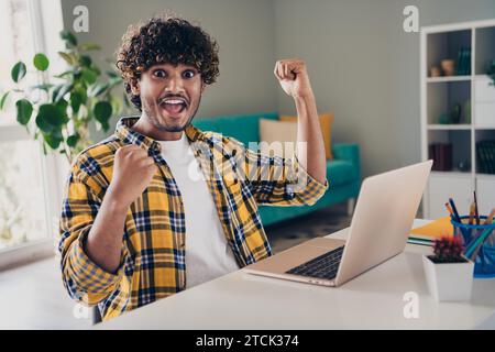 Photo of crazy excited cheerful guy it specialist hacker with raised hands fists rejoice completed task work workplace indoors Stock Photo