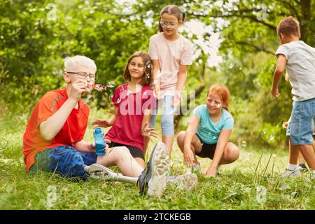 Disabled boy blowing bubbles with friends while sitting at park Stock Photo