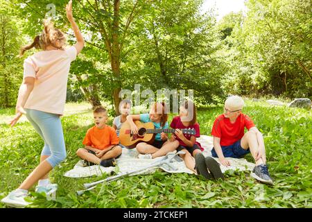 Girl playing guitar while sitting with friends on blanket at park Stock Photo