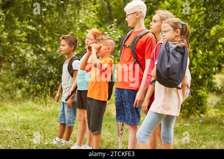 Curious boy looking through binoculars while standing with friends at park Stock Photo