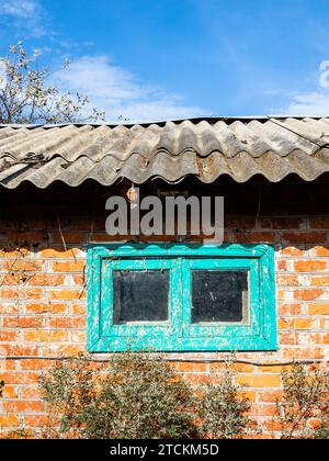 brick barn with dirty small window in green wooden frame covered with slate roof in village on sunny autumn day Stock Photo