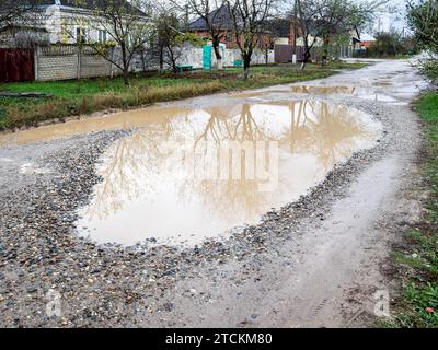 large dirty rain puddle on road in village on autumn day Stock Photo