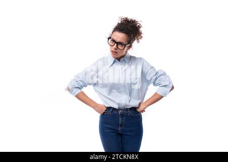 an amazing young brunette curly-haired manager woman is dressed in a loose-fitting light blue shirt tucked into jeans Stock Photo