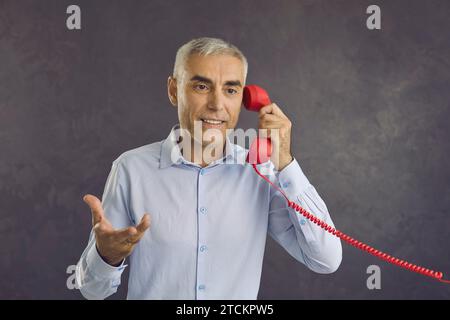 Portrait of serious senior man talking to someone on red retro landline telephone Stock Photo