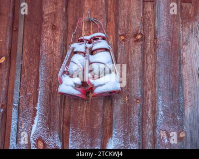 Two old kerosene lamps covered with snow hang on a wooden wall. Winter decoration. Stock Photo