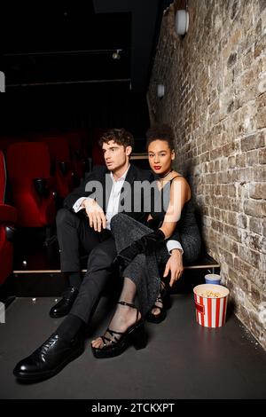 attractive multiracial couple in black elegant attires sitting at cinema on date on Valentines day Stock Photo