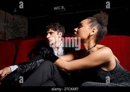 young alluring multiracial couple in black dress and suit sitting together on date at cinema Stock Photo