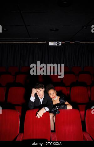 appealing multicultural stylish couple in evening black attires sitting on red chairs at cinema Stock Photo