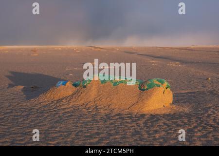 Plastic soup; green plastic bottle washed up on the beach, almost disappeared under the sand Stock Photo