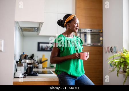 Portrait of a smiling mature woman standing in her kitchen  drinking coffee Stock Photo