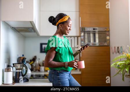 Smiling woman using smartphone in the kitchen at home Stock Photo