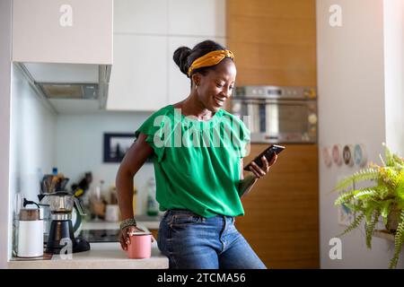 Smiling woman using smartphone in the kitchen at home Stock Photo