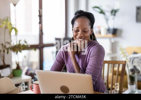 Smiling woman working on laptop at home Stock Photo
