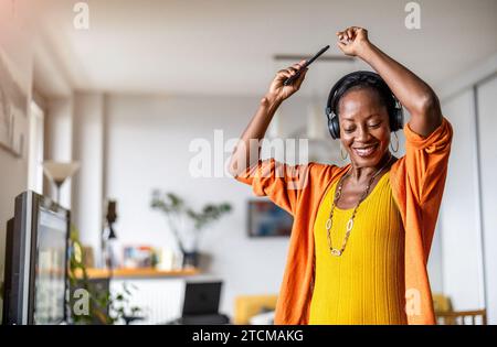 Woman listening to music with headphones connected to her smartphone in the living room at home Stock Photo