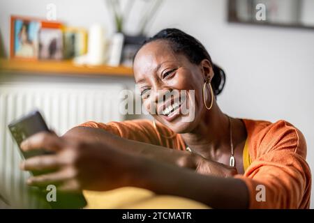 Beautiful woman using mobile phone while relaxing on sofa at home Stock Photo