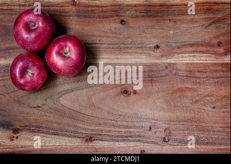 Three red apples on a wood cutting board with copy space to the right Stock Photo