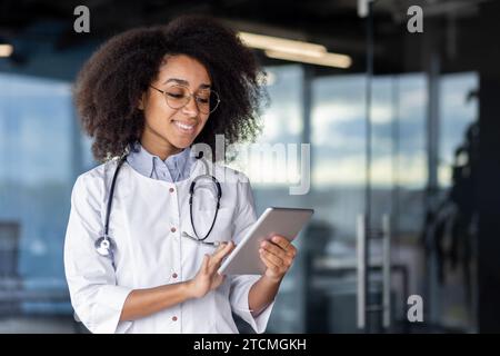 Satisfied female doctor holding a tablet in her hands, standing in a modern private clinic, happy with her choice of job. Stock Photo