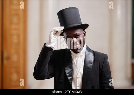 Waist up portrait of young Black gentleman wearing top hat smiling at camera in palace and giving well mannered bow Stock Photo