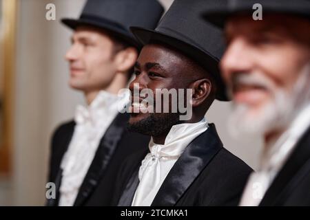 Side view portrait of smiling Black gentleman wearing classic top hat and tuxedo standing in row Stock Photo