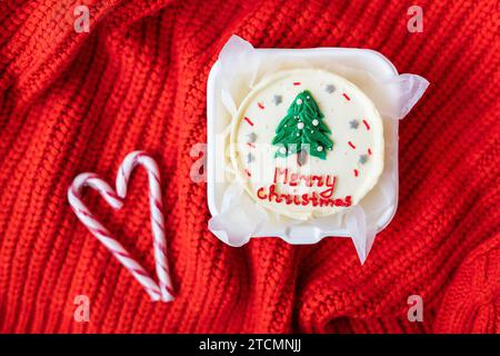 Christmas cupcake with a candy cane heart on a red knitted background. Merry christmas cake inscription Stock Photo