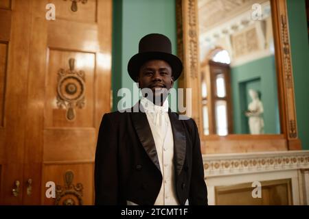 Waist up portrait of smiling Black gentleman wearing top hat looking at camera in palace Stock Photo