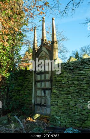 An unusual carved wooden spired gate built into an old mossy stone wall in a leafy corner of Totley, Sheffield. Stock Photo