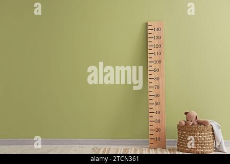 Basket with toy bear and stadiometer near green wall in room Stock Photo