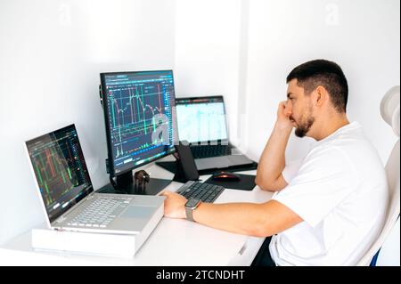 Focused male trader sitting at home at his work desk, trading on the stock exchange, analyzing the future of cryptocurrency, assessing risks, working online Stock Photo