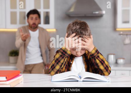 Father getting annoyed while son doing his homework in kitchen, selective focus. Dyslexia problem Stock Photo