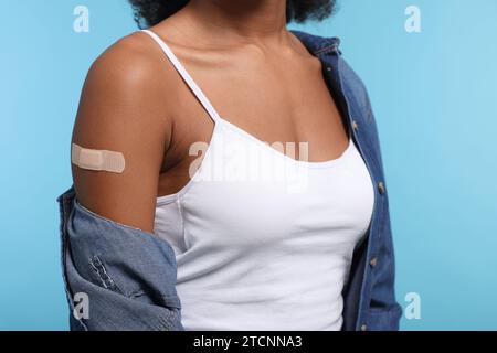 Young woman with adhesive bandage on her arm after vaccination against light blue background, closeup Stock Photo