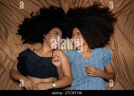 Half-closed portrait of two women lying down with their curly hair and power spread on the floor cloth. Solid friendship concept. Stock Photo