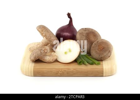 Fresh shiitake mushrooms, various onions on a wooden cutting board isolated on white background. Fungi recipes and medicinal herbs Stock Photo