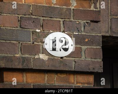 Number 12 on an exterior house wall. The twelve is part of an address. The metal plate is white with black figures. The design is vintage and old. Stock Photo