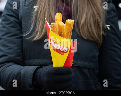Churros dessert with sugar and cinnamon topping. A woman holding the sweet snack in front of her. Churros are fried dough from the Spanish cuisine. Stock Photo