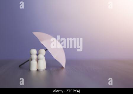 Umbrella and wooden dolls with copy space. Family protection and insurance coverage concept. Stock Photo