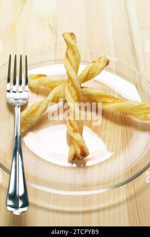 Puff pastry sticks on a glass transparent plate over pine wood table Stock Photo