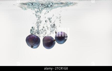 Three figs sinking into water isolated against white background Stock Photo