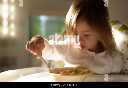 Two years old eats porridge by herself with a spoon. Child development concept Stock Photo