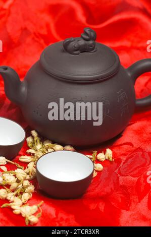 Jasmine tea dry flowers, pot and two cups, over red silk tablecloth Stock Photo