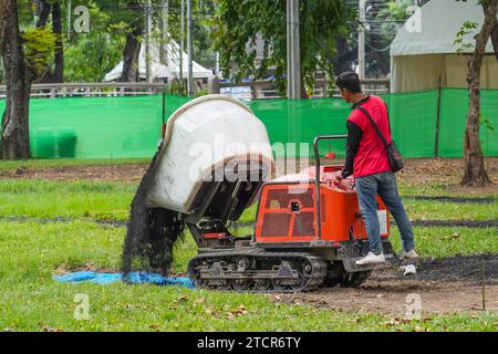 Worker operates special equipment, pours out soil for planting in the back of a mini loader on tracks. Tough heavy duty dump truck dirt construction r Stock Photo