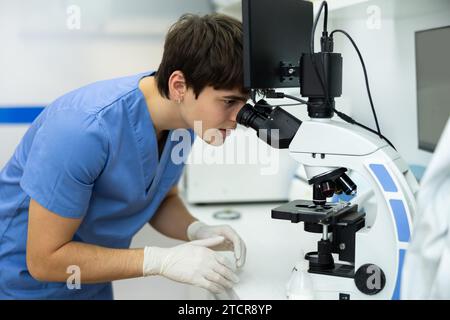 Young veterinarian using microscope to examine blood samples of animal patient Stock Photo