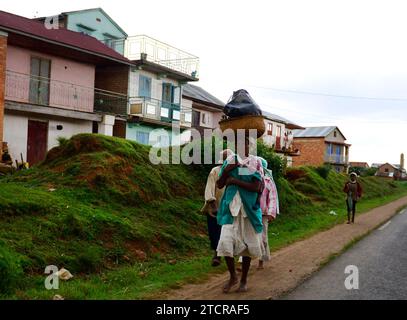 A Malagasy woman carrying a heavy bag on her head along the road in central Madagascar. Stock Photo