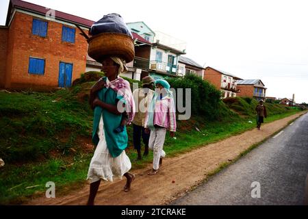 A Malagasy woman carrying a heavy bag on her head along the road in central Madagascar. Stock Photo