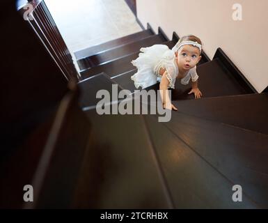 Portrait of a tiny adorable little girl climbing the stairs in her home Stock Photo