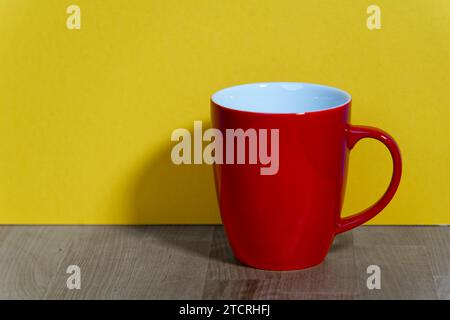 an empty red ceramic coffee mug with a handle stands on a natural wooden board in front of a colored background with real shadows Stock Photo