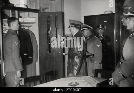 During his visit to his Leibstandarte, Adolf Hitler is seen inspecting the uniform of one of the soldiers, with SS-Obergruppenführer Josef Dietrich standing beside him. This moment highlights Hitler's attention to detail and the discipline he expected within his personal bodyguard unit. The inspection, conducted in the presence of a high-ranking SS officer, underscores the importance of the SS in the Nazi hierarchy and the emphasis placed on their appearance, loyalty, and role as a symbol of the regime's power and order. Stock Photo