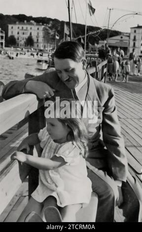 Adolf Hitler is captured in a moment of calm, accompanied by Helga Goebbels, the young daughter of Joseph Goebbels. This image contrasts with his typical public and political appearances, showing a more private side. The presence of Helga aims to present Hitler in a more relatable and softer light, a tactic used in Nazi propaganda to humanize him and portray him as a benevolent figure. Stock Photo