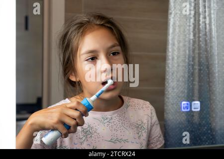 happy little girl brushes her teeth in front of a mirror in the bathroom. Morning routine. Hygiene. Stock Photo