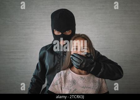 Terrorist and scared little hostage girl with Closed mouth on dark background. The concept of kidnapping. Stock Photo