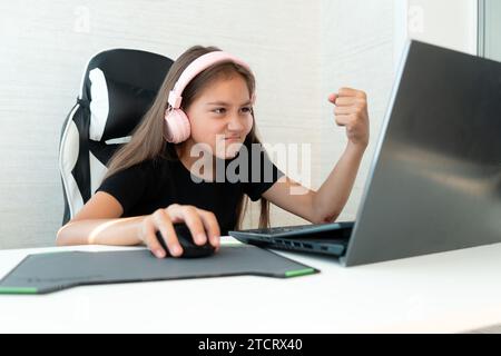 A teenage girl in pink headphones is playing computer games on a white background. A negative emotion on the face. the child gamer shows his fist at t Stock Photo